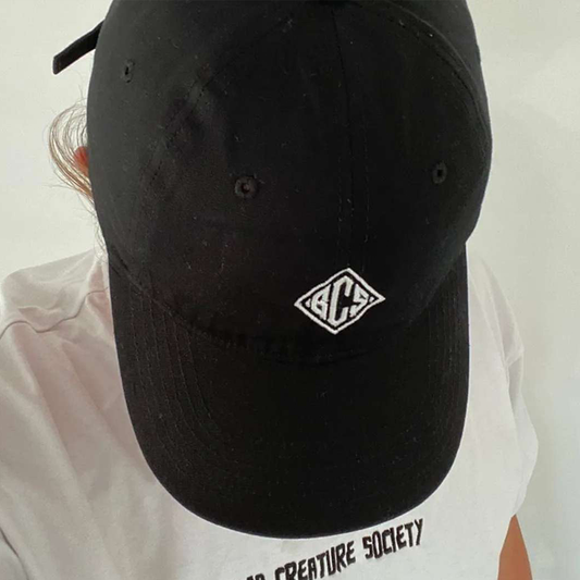 Black cap with a logo worn by a person wearing a white shirt with text.