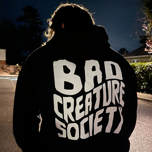 Person wearing a hoodie with 'Bad Creature Society' text at night.